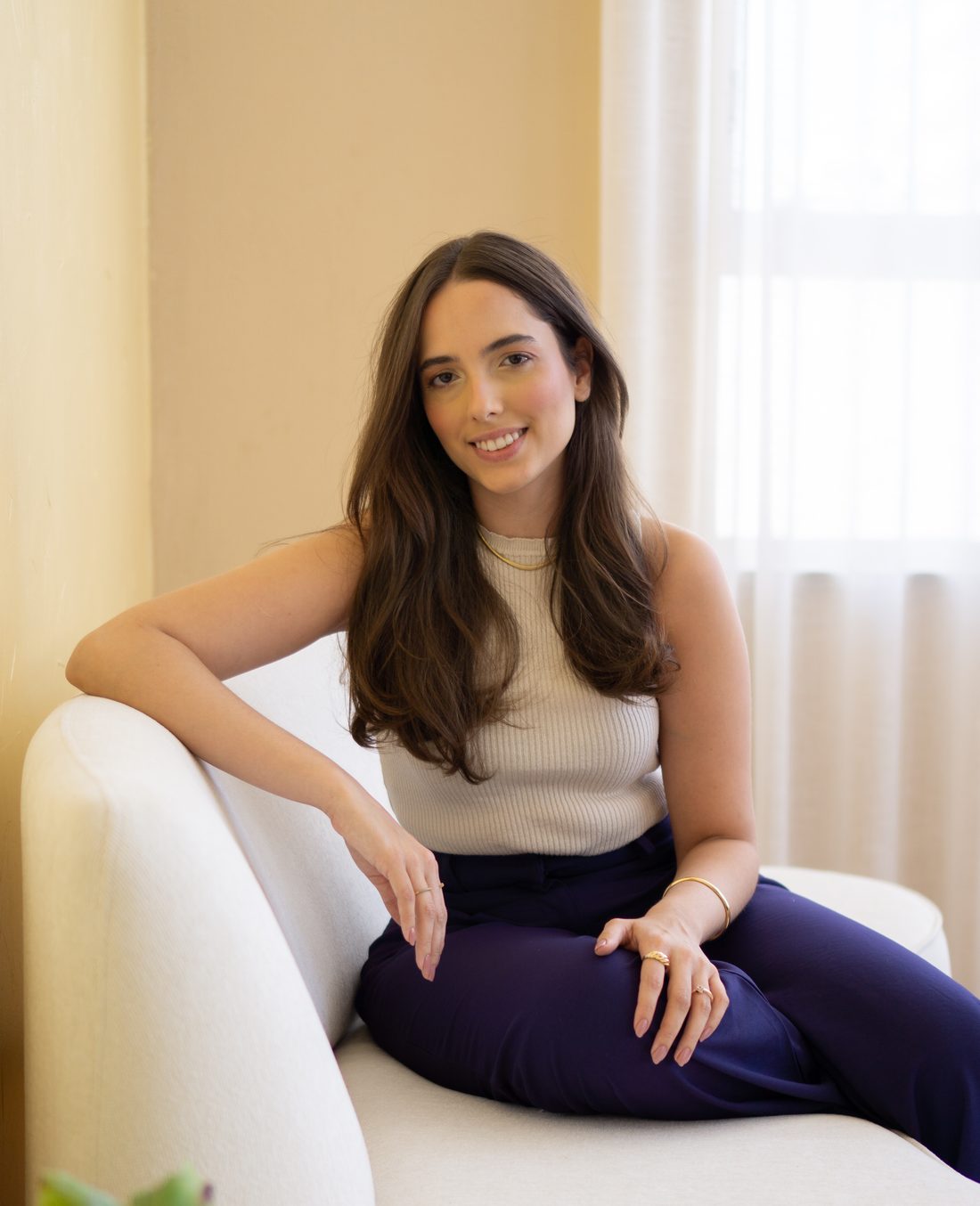 Luiza Barbosa, psicóloga, sentada em um sofá claro e sorrindo
